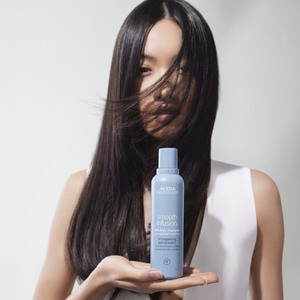 Model mit glatten langen Haaren und Shampoo in der Hand Aveda Smooth Infusion Pflegeritual
